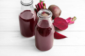 Two glass bottles with fresh smoothie and beets on wooden table