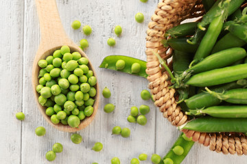 Wicker basket and spoon with fresh green peas on light wooden table