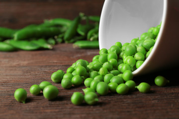 Bowl and scattered green peas on wooden table
