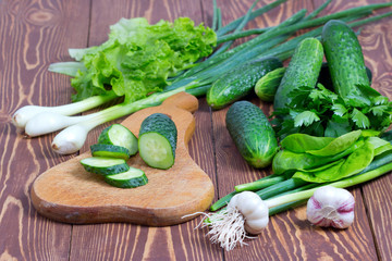 Свежие огурцы и зелень на деревянной разделочной доска,фон деревянный
