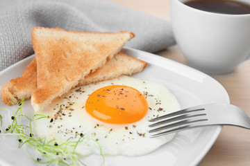 Plate of homemade over easy fried egg with toasts and cup of tea on table