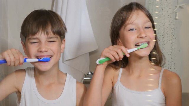 Children brush their teeth. A boy and a girl brush their teeth in the bathroom. The children clean their teeth.