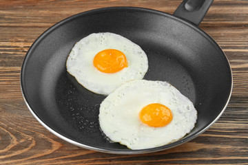 Frying pan with tasty over easy eggs on wooden table