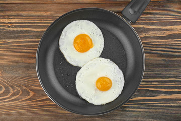 Frying pan with tasty over easy eggs on wooden table