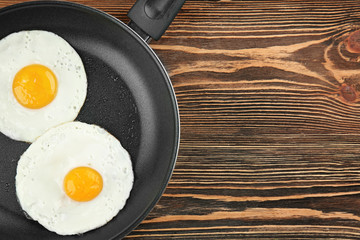 Frying pan with tasty over easy eggs on wooden table