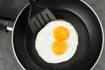 Homemade over easy eggs with spatula in frying pan on dark background