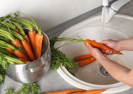 Woman washing fresh carrots in kitchen sink
