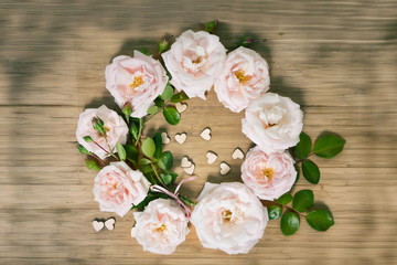 pink roses wrealh with small wooden hearts on the wooden table, top view with copy space