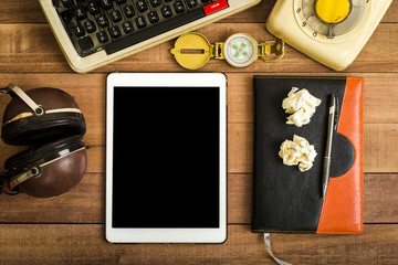Top view of tablet with black space on the wood table with notebook, typewriter, old telephone and earphone