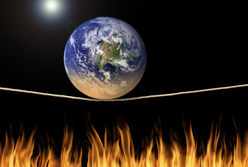Earth balancing on tightrope over fire flames with the sun in background representing environmental problems, disaster, climate change and death. Some elements provided by Nasa.