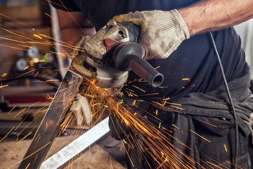 Close-up A young man welder wearing a black T-shirt is grinds metal with an angle grinder in the...