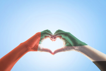 UAE, United Arab Emirate national flag pattern on people's hands in heart shape on blue mint sky background