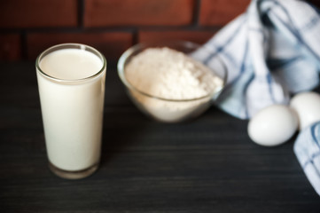 The process of preparation in detail. Cooking, kneading dough. A glass of milk, 2 eggs, a saucer with flour and a blue napkin on a black wooden table