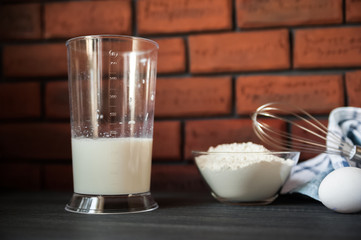 The process of preparation in detail. Cooking, kneading dough. A glass of milk, 2 eggs, a saucer with flour and a blue napkin on a black wooden table