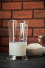The process of preparation in detail. Cooking, kneading dough. A glass of milk, 2 eggs, a saucer with flour and a blue napkin on a black wooden table