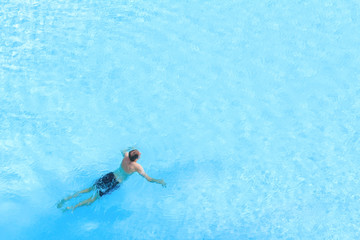 high angle view of one man swimming in a blue swimming pool on a sunny day.