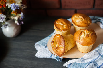 Fresh cooked cupcakes. Delicious homemade muffins with a pear. Cupcakes with a blue napkin on a dark black wooden table. Wildflowers, camomiles and homemade cakes