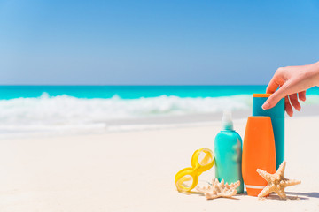 Suncream bottles, goggles, starfish on white sand beach background ocean