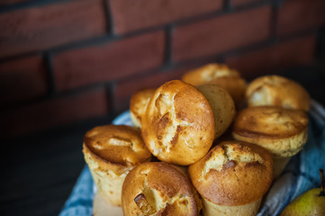 Fresh cooked cupcakes. Delicious homemade muffins with a pear. Cupcakes with a blue napkin on a dark black wooden table. Wildflowers, camomiles and homemade cakes