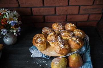 Fresh cooked cupcakes. Delicious homemade muffins with a pear. Cupcakes with a blue napkin on a dark black wooden table. Cupcakes, muffins sprinkled with powdered sugar on the background of a red bric