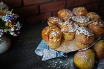 Fresh cooked cupcakes. Delicious homemade muffins with a pear. Cupcakes with a blue napkin on a dark black wooden table. Cupcakes, muffins sprinkled with powdered sugar on the background of a red bric