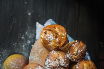 Fresh cooked cupcakes. Delicious homemade muffins with a pear. Cupcakes with a blue napkin on a dark black wooden table. Cupcakes, muffins sprinkled with powdered sugar on the background of a red bric