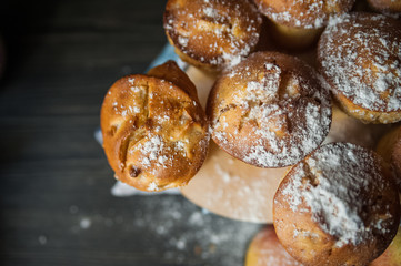 Fresh cooked cupcakes. Delicious homemade muffins with a pear. Cupcakes with a blue napkin on a dark black wooden table. Cupcakes, muffins sprinkled with powdered sugar on the background of a red bric