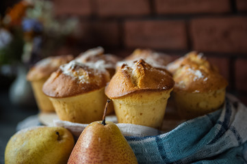 Fresh cooked cupcakes. Delicious homemade muffins with a pear. Cupcakes with a blue napkin on a dark black wooden table. Cupcakes, muffins sprinkled with powdered sugar on the background of a red bric
