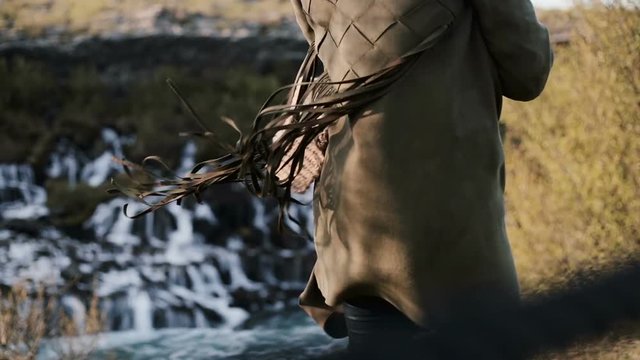 Close-up view of Barnafoss waterfall in Iceland and female back. Fringe from jacket of young woman waves on wind.