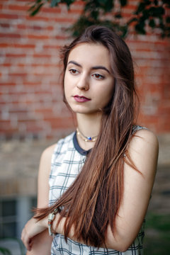 Closeup portrait of beautiful pensive young middle eastern Caucasian jewish woman with long dark hair and black brown eyes looking away. Girl in white plaid shirt against brick wall. Natural beauty