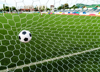Soccer football in Goal net with green grass field.