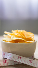 potato chips in a white bowl and measuring cable on wooden table