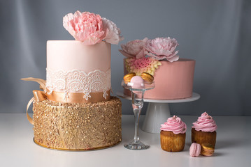 Luxury wedding table with a beautiful pink cake decorated with mastic pink rose and gold on gray...
