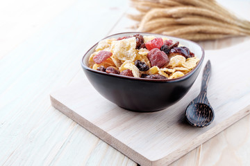 cornflakes and dry berry fruits in a brown bowl on a wooden background.