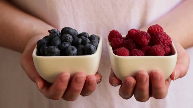 Blueberries and raspberries, female hands with berry fruit in crockery