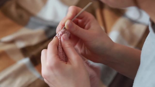 A young woman in a gray T-shirt knits a scarf crochet with pink thread of natural wool, the top view