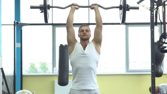 Muscular man on strength training in the gym. Athlete makes triceps exercise with a barbell