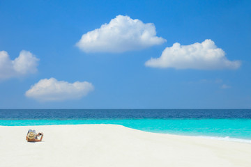 Fototapeta na wymiar A woman lying and relaxing on a white sand beach with turquoise sea and blue sky in the Maldives.