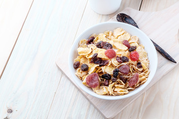 cornflakes and dry berry fruits in a white bowl on a wooden background.
