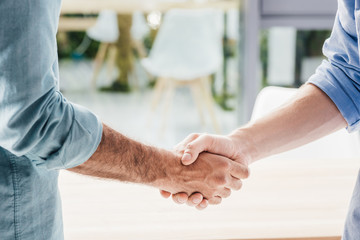 cropped shot of businessmen shaking hands after meeting in office