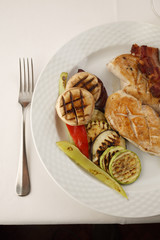 Chicken with bacon and grilled vegetables arranged on a plate, Traditional dish in elegant setting, Selective focus with soft light
