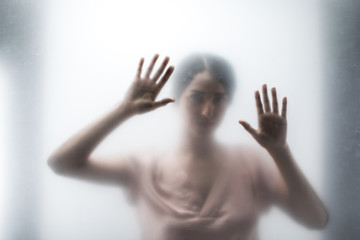 Silhouette of woman looking through the glass and touching it with hands