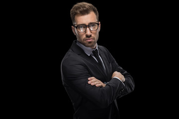 handsome businessman posing with crossed arms in eyeglasses and black suit, isolated on black