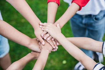 Cropped shot of children stacking hands while standing on green grass