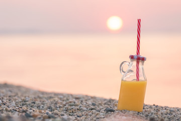 Glass bottle of fresh orange juice on beach at sunset over sea