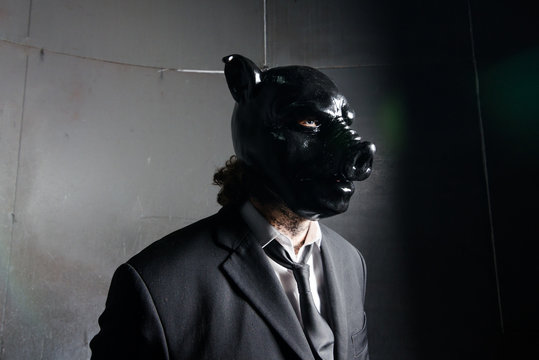 A corporate man in a dirty scruffy suit wearing a black pigs mask in a dark sinister background, photographed with moody cinematic lighting. evil dirty corporate pigs.