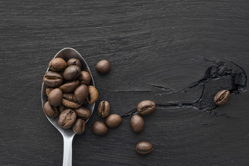 Spoonful of coffee beans on black wooden background