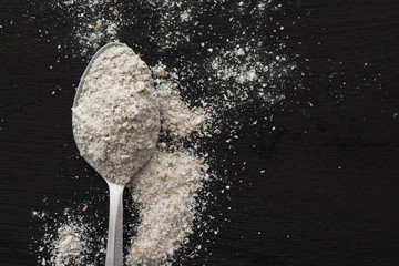 Spoonful of flour on black wooden background