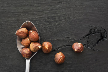 Spoonful of hazelnuts on black wooden background