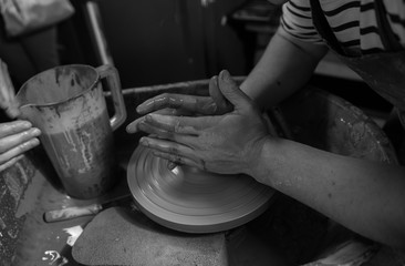 Hands working on a spinning pottery wheel, making pottery out of clay mud. close up photograph with a shallow depth of field.
